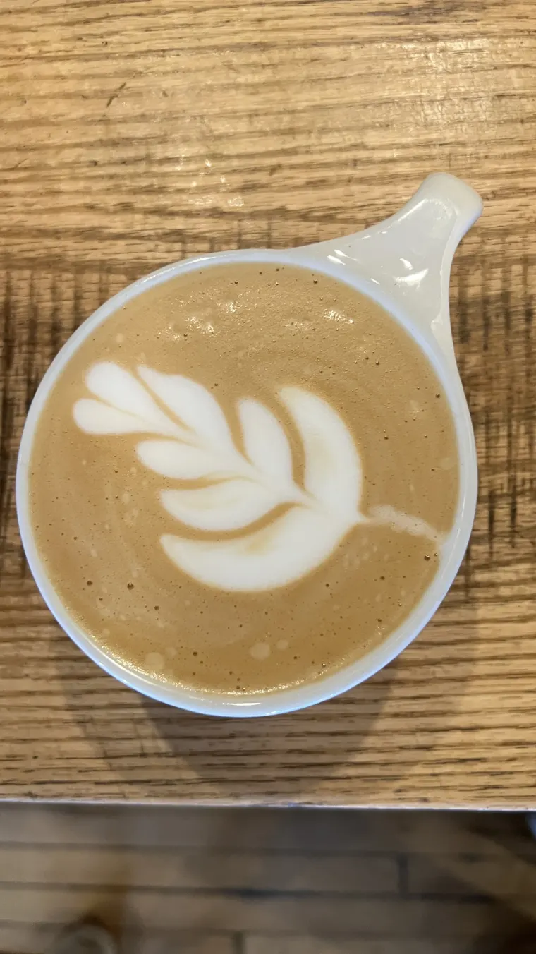 A cup of coffee with leaf-shaped latte art on a wooden table
